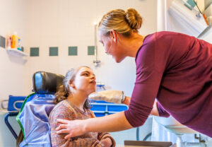 A young disabled girl in a wheelchair receiving support from a female carer within a bathroom environment