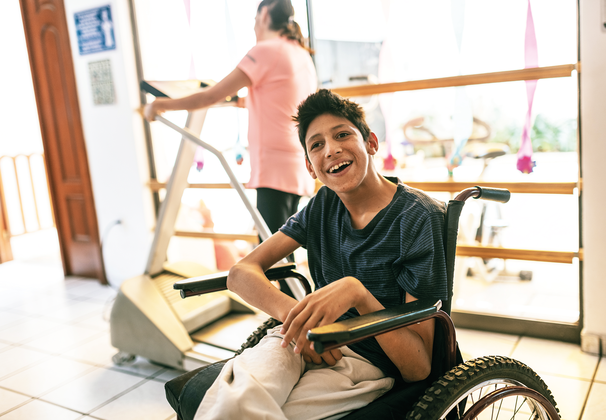 A young smiling disabled boy in a wheelchair within a gym like environment