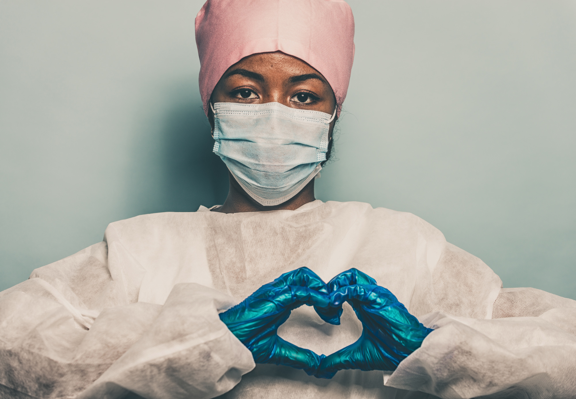 A female nurse attired in appropriate PPE and posing in a loving way