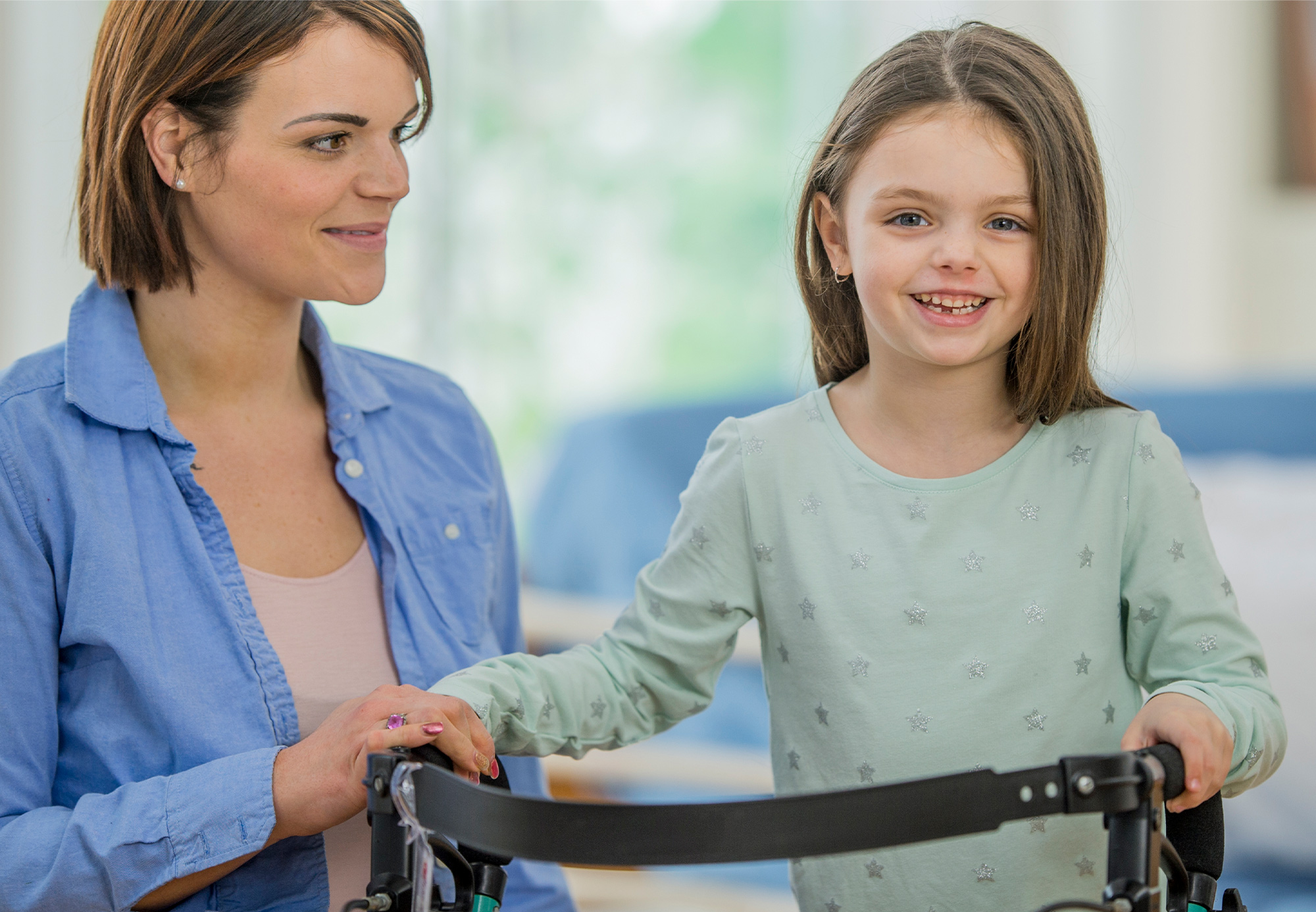 A young disabled girl smiling on a walker next to her female carer